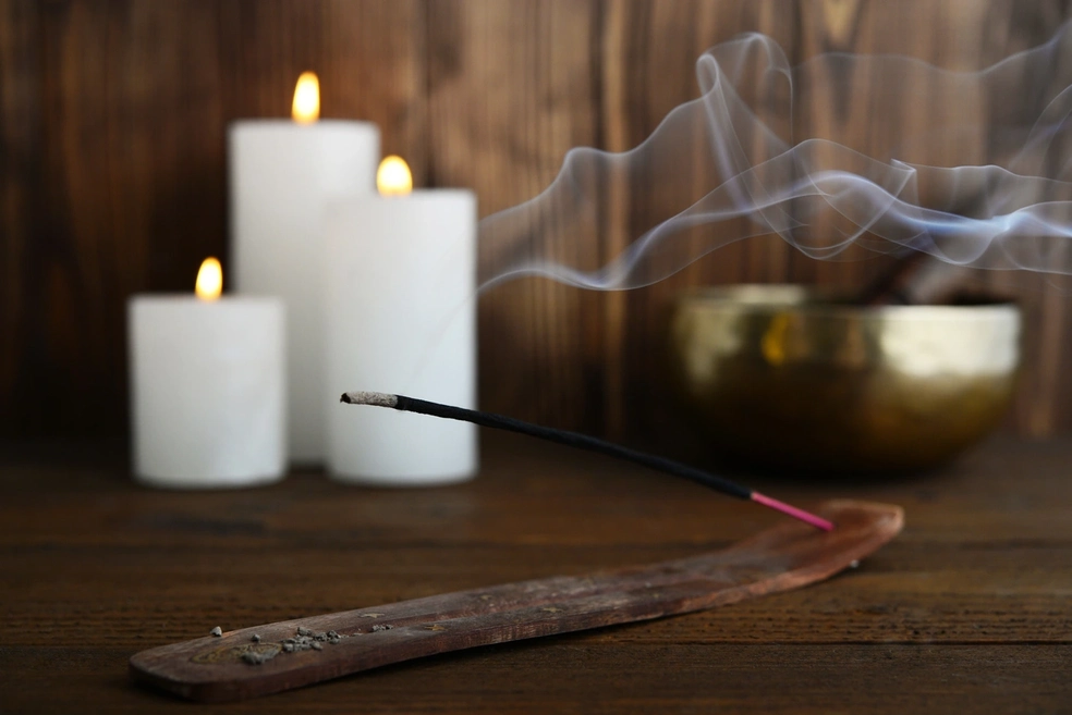 A burning incense stick next to candles on a table.